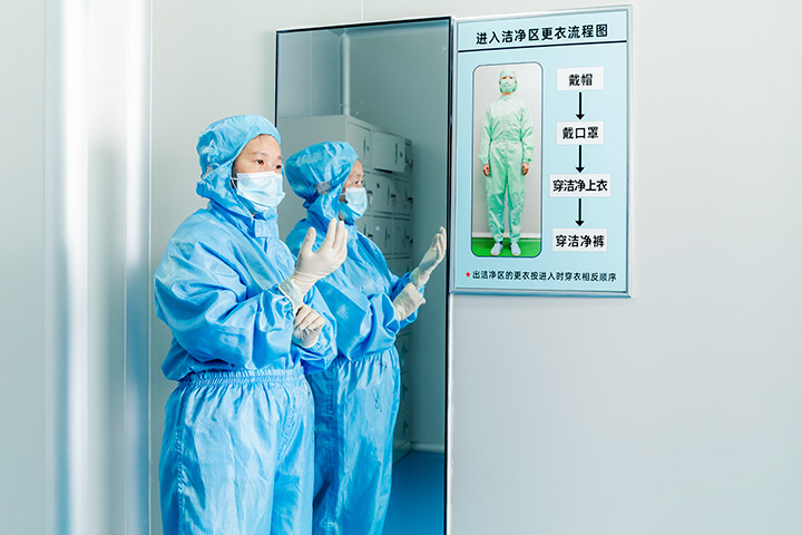 a female worker is wearing gloves, masks, and anti bacteria uniform before entering the cleanroom