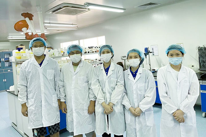 5 people in white uniform standing together in a lab equipped with equipment and devices